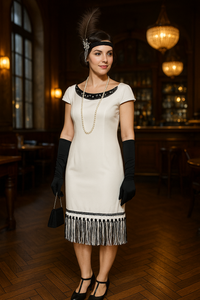 Cremeweißes Fransenkleid mit schwarzem Perlenbesatz am Ausschnitt und Saum. Schwarze Armhandschuhe, lange weiße Perlenkette, Feder-Kopfschmuck mit Schwarz und Silber, kleine schwarze Clutch, T-Strap-Schuhe angepasst in Schwarz mit dezenten Blütenapplikationen. Größe 40
