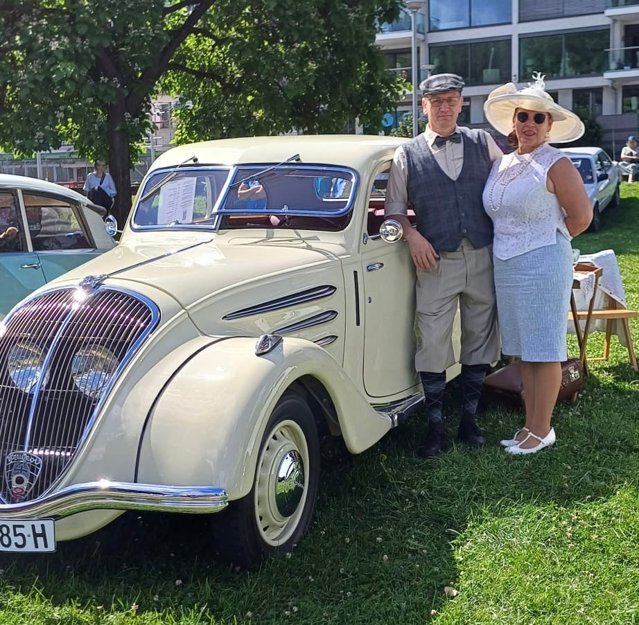 Damen-und Herrenmodell in Oldtimerkleidung vor einem Oldtimer Auto.