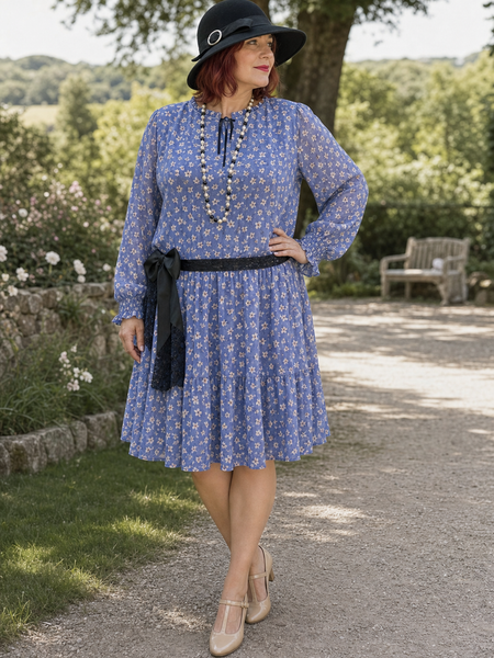 Plus-Size Dame in blauem 1920er Jahre Tageskleid Gr. 50 mit schwarzem Hut, Perlenkette und Schleife im Park