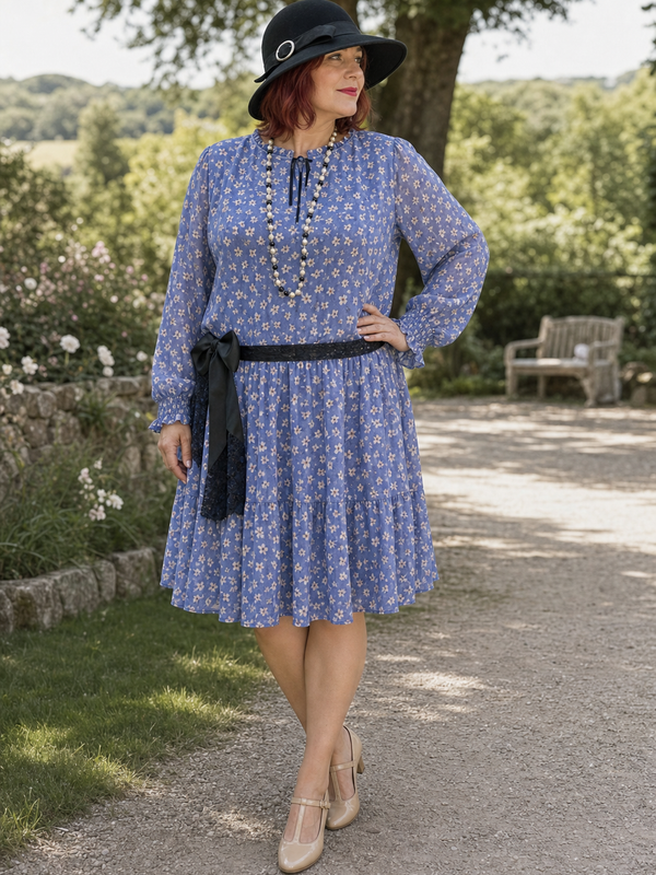Plus-Size Dame in blauem 1920er Jahre Tageskleid Gr. 50 mit schwarzem Hut, Perlenkette und Schleife im Park