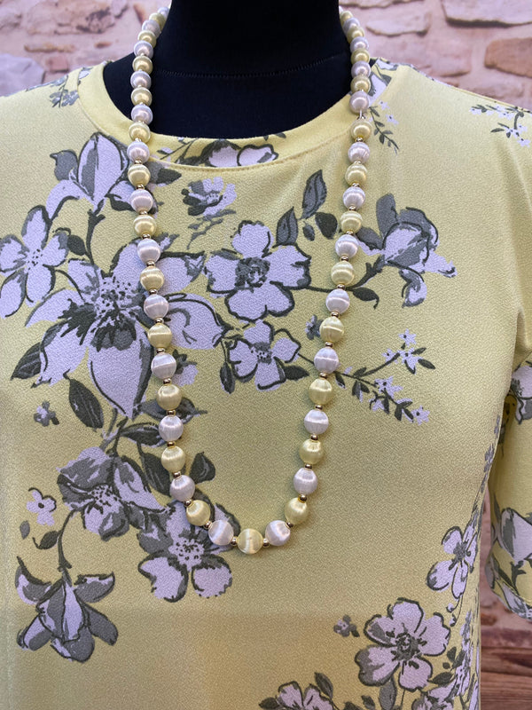 „Detailansicht vom gelben 1920er Jahre Kleid mit Perlenkette und zartem Blumenmuster“