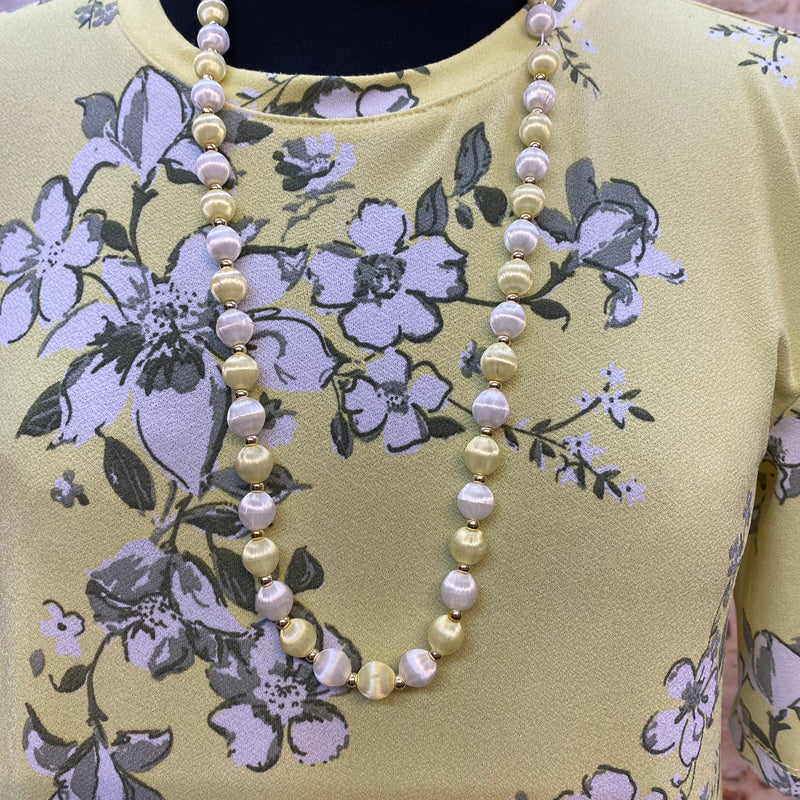 „Detailansicht vom gelben 1920er Jahre Kleid mit Perlenkette und zartem Blumenmuster“