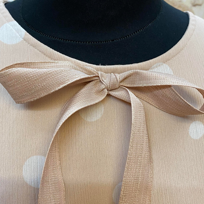 „Detail vom Ausschnitt mit roséfarbener Bindeschleife am gepunkteten 20er Jahre Kleid“