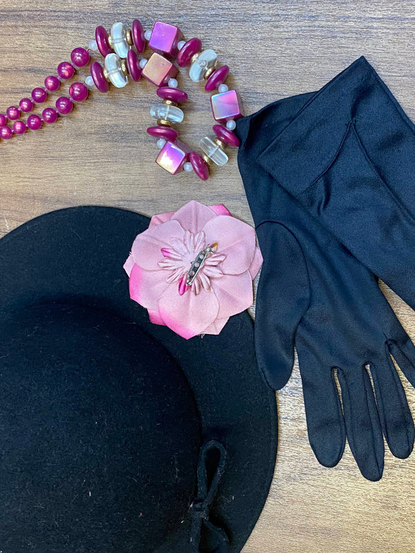„Accessoires zum 1920er Jahre Damen-Outfit mit schwarzem Hut, rosa Blüte, Handschuhen und Kette“