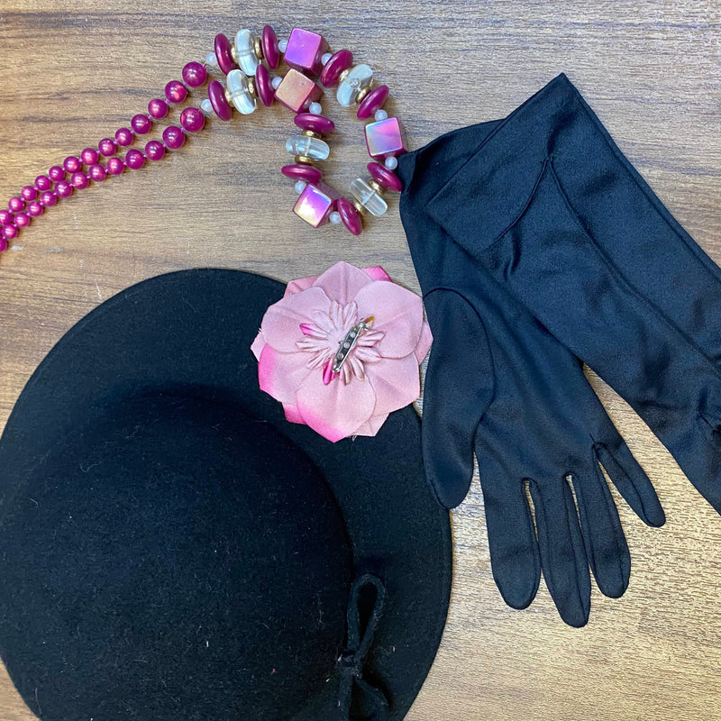 „Accessoires zum 1920er Jahre Damen-Outfit mit schwarzem Hut, rosa Blüte, Handschuhen und Kette“
