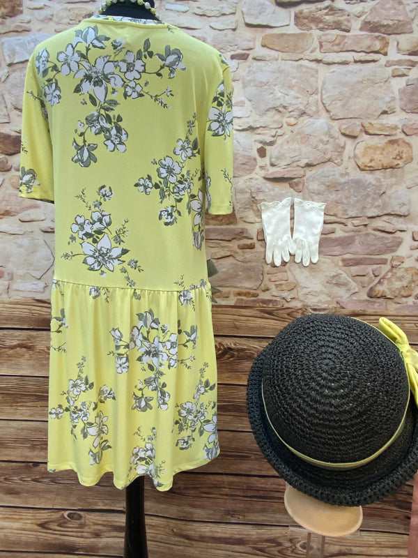 „Rückansicht vom gelben floralen Tageskleid im 1920er Jahre Stil mit Hut und weißen Handschuhen“
