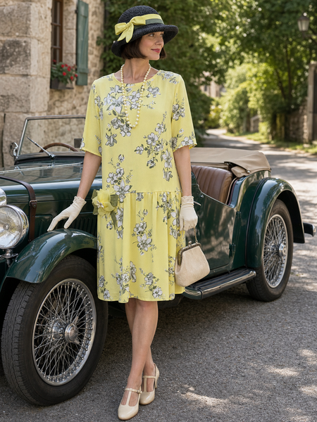 Model in gelbem 1920er Tageskleid Gr. 38 mit schwarzem Hut, Perlenkette und Handschuhen neben einem Oldtimer