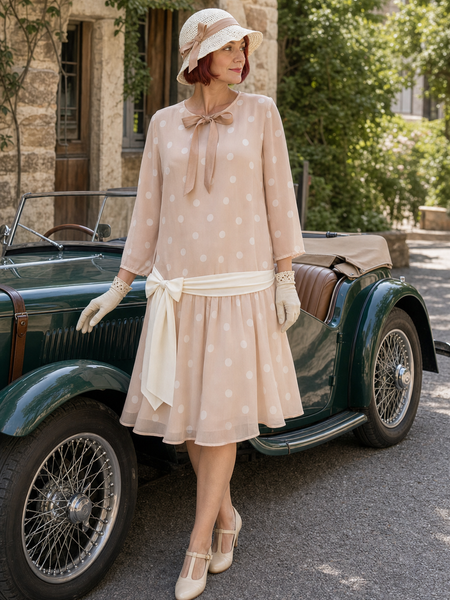 Model in rosebeigem 1920er Tageskleid Gr. 40 mit weissem Tupfenmuster, Hut und Handschuhen neben einem Oldtimer