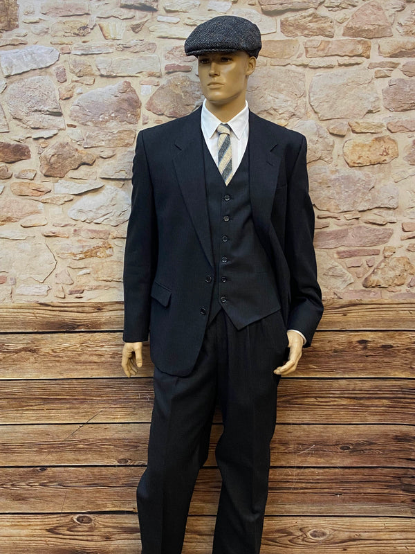 „Vintage Herrenset im 20er Jahre Stil mit anthrazitfarbenem Wollanzug, Weste, Bundfaltenhose, weißem Hemd, Wollkrawatte und Tweed-Schiebermütze.