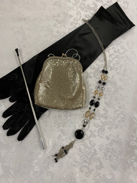 „20er-Jahre Damen-Set mit langen schwarzen Handschuhen, silberfarbener Zigarettenspitze, goldener Vintage Mesh-Abendtasche und langer Perlenkette.“