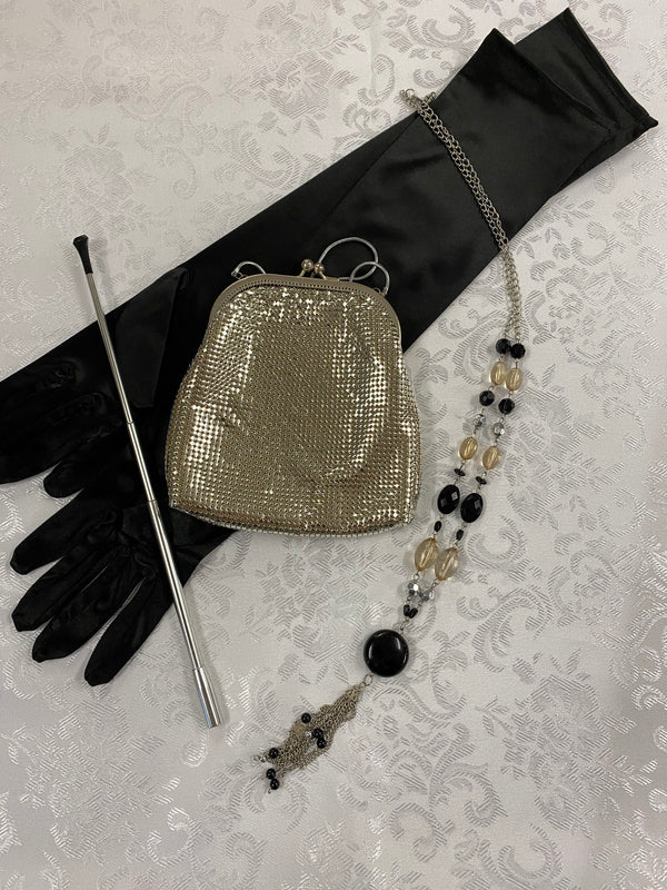„20er-Jahre Damen-Set mit langen schwarzen Handschuhen, silberfarbener Zigarettenspitze, goldener Vintage Mesh-Abendtasche und langer Perlenkette.“