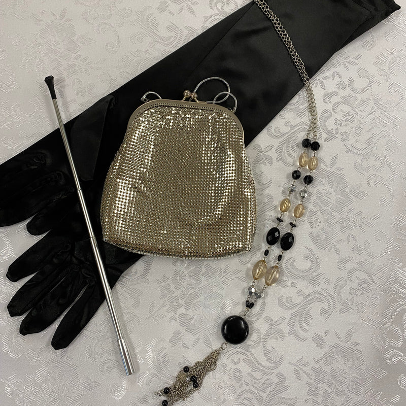 „20er-Jahre Damen-Set mit langen schwarzen Handschuhen, silberfarbener Zigarettenspitze, goldener Vintage Mesh-Abendtasche und langer Perlenkette.“