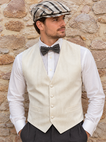 20er Jahre Herren Outfit mit cremefarbener Weste, weißem Hemd, Fliege und dunkelgrauer Hose vor Steinwand