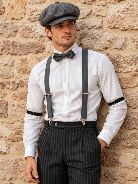 20er Jahre Herren Outfit mit gestreifter Hose, Hemd, Hosenträgern, Fliege und Schiebermütze vor Steinwand