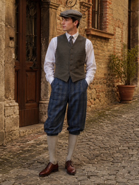 KI-generiertes Bild eines Herren-Outfits im 20er-Jahre-Stil mit blau karierter Knickerbocker, grauer Weste, weißem Hemd, Krawatte, Schiebermütze und Kniestrümpfen in historischer Gassen-Umgebung