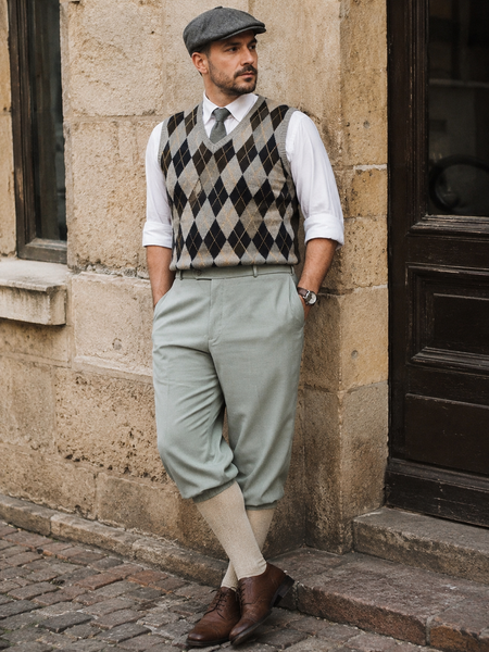 KI-generiertes Bild eines Herren-Outfits im 20er-Jahre-Stil mit salbeigrüner Knickerbocker, Rautenpulli, Schiebermütze und Kniestrümpfen in realer historischer Umgebung