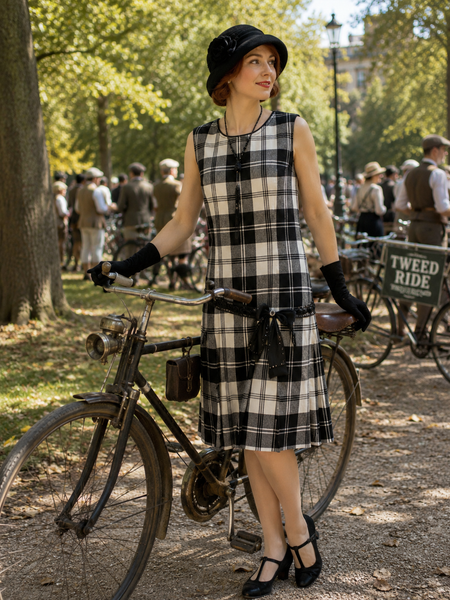 „Kariertes 20er-Jahre Tageskleid auf einem Model beim Tweed Ride im Park mit schwarzem Hut, Handschuhen und historischem Fahrrad“