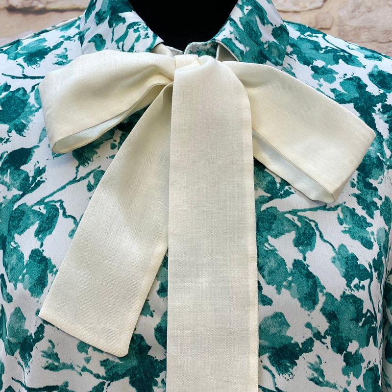 „Detailaufnahme 1920er Tageskleid mit großer cremefarbener Schleife und grünem Blumenmuster“