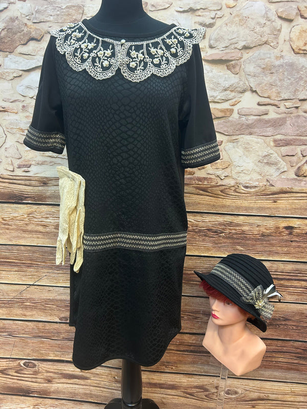 Komplettes 20er-Jahre Outfit: schwarzes Kleid mit Perlenspitze, schwarzer Cloche-Hut mit Feder, cremefarbene Spitzenhandschuhe.