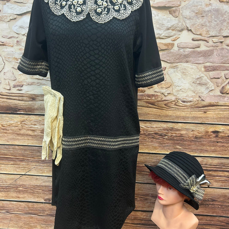 Komplettes 20er-Jahre Outfit: schwarzes Kleid mit Perlenspitze, schwarzer Cloche-Hut mit Feder, cremefarbene Spitzenhandschuhe.