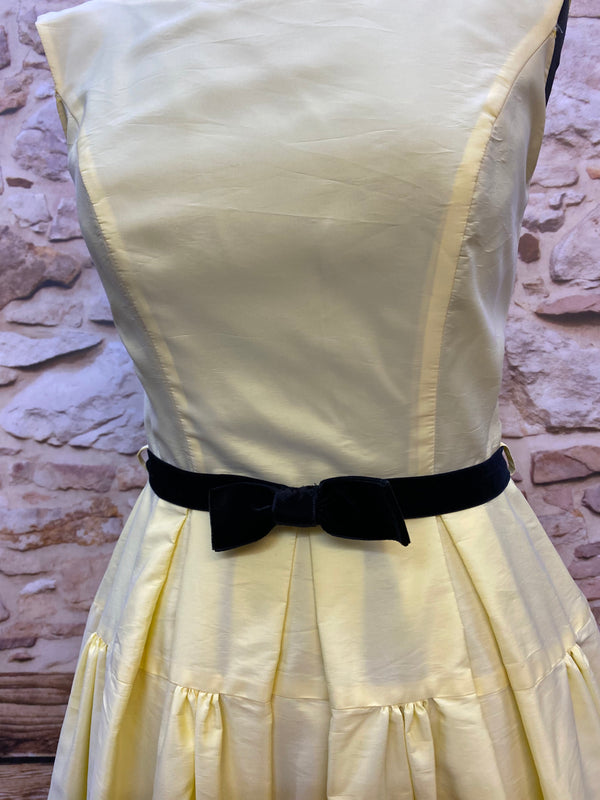 „Detailansicht vom hellgelben Swing Kleid im 50er Jahre Stil mit schwarzem Samtgürtel und Schleife“