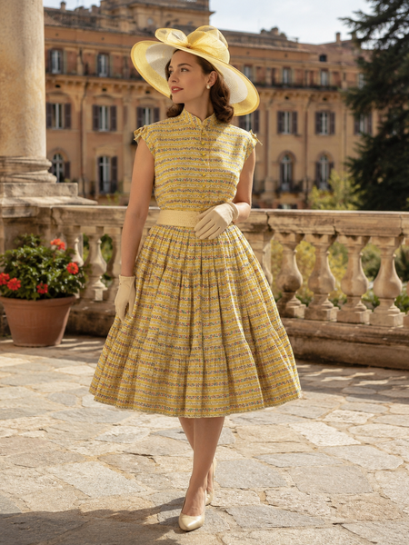 Original 50er Jahre Outfit mit gelbem tellerweitem Kleid, großem Hut, beigen Handschuhen und Gürtel in historischer Umgebung.