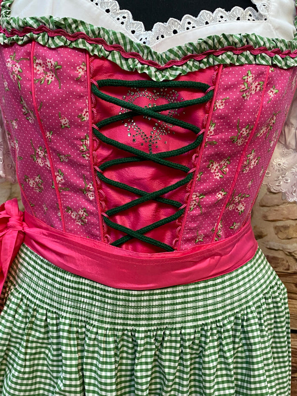 „Detailaufnahme der grünen Schnürung und des floralen Mieders beim pink-grünen Dirndl“