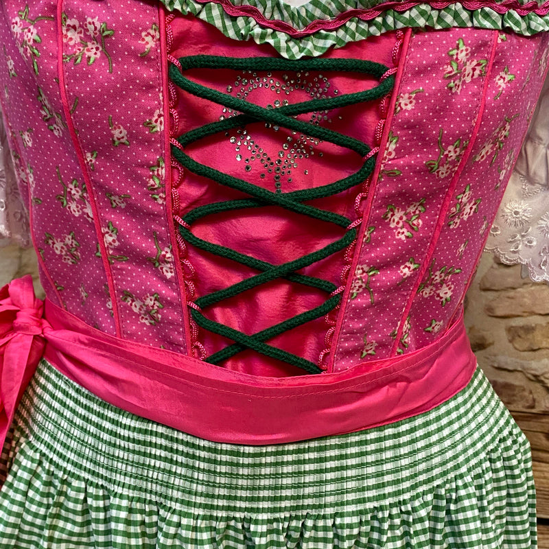 „Detailaufnahme der grünen Schnürung und des floralen Mieders beim pink-grünen Dirndl“
