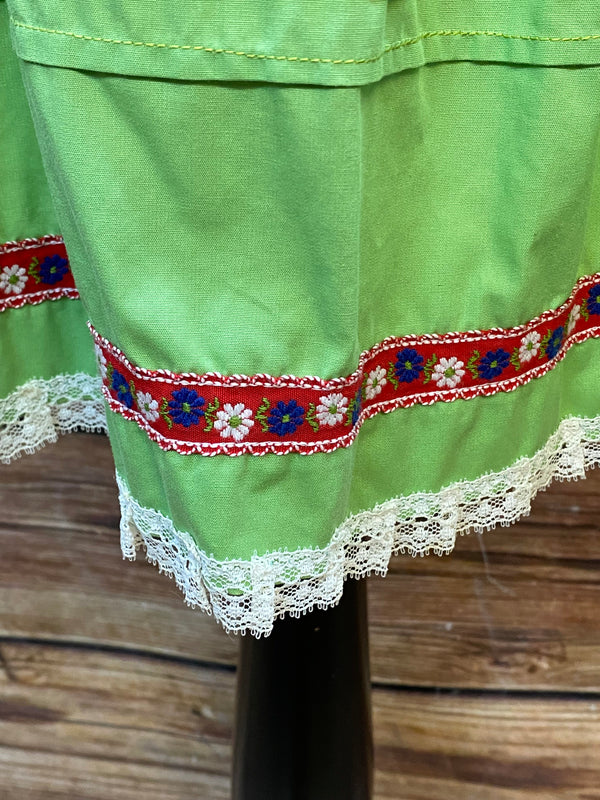 „Detailaufnahme grüne Trachten Schürze mit floraler Borte in Rot und Blau“