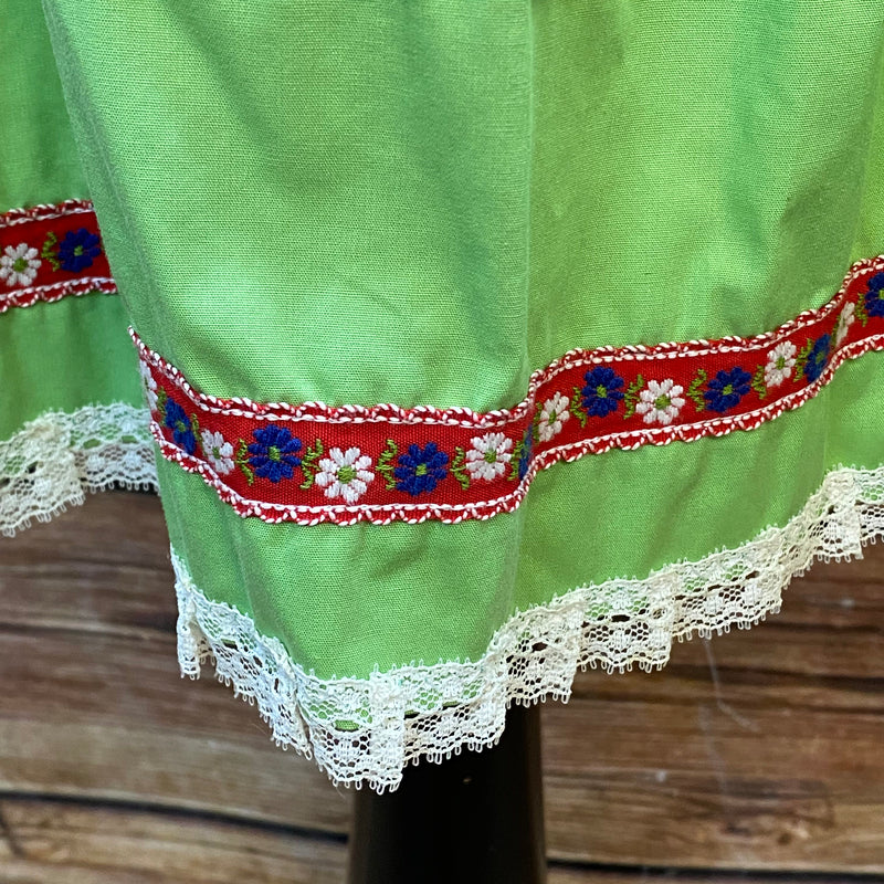 „Detailaufnahme grüne Trachten Schürze mit floraler Borte in Rot und Blau“