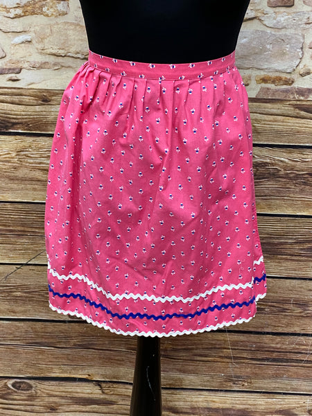 „Rosa Vintage Dirndl-Schürze  mit Blumenmuster, Zierborten in Weiß und Blau, Baumwolle, Schleifenverschluss.“