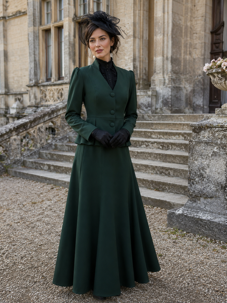 Grünes Damenkostüm im historischen Stil mit langem Rock, schwarzer Bluse, Hut und Handschuhen vor historischer Schlosskulisse.