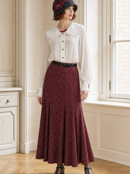 Frau im Oldtimer-Outfit der 20er-Jahre mit weißer Vintagebluse, burgunderrotem Blumenrock und grauem Cloche-Hut.