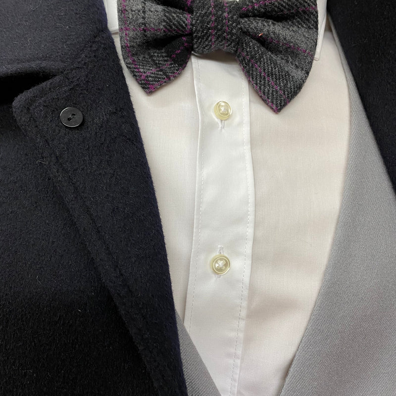 „Detailaufnahme der grauen Handmade-Fliege am weißen Hemd unter schwarzem Mantel – 20er Jahre Stil.“