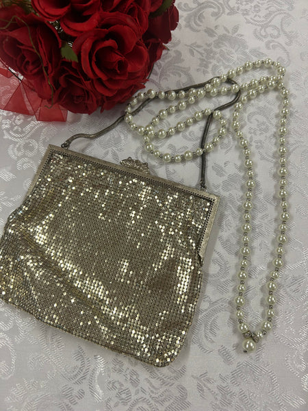 „Vintage Abendtasche aus silberfarbenem Metall-Mesh mit Perlenkette, neben roten Rosen“