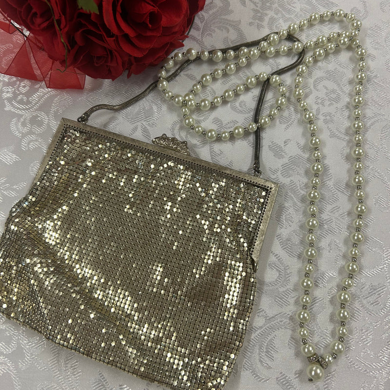 „Vintage Abendtasche aus silberfarbenem Metall-Mesh mit Perlenkette, neben roten Rosen“