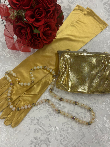 Goldfarbene Vintage-Handtasche mit Perlenkette und langen Satin-Handschuhen auf weißem Hintergrund.