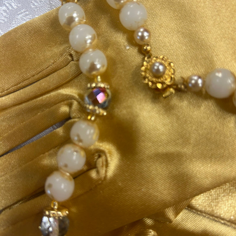 Detailaufnahme einer goldfarbenen Perlenkette mit Kristallelementen auf Satin-Handschuhen.