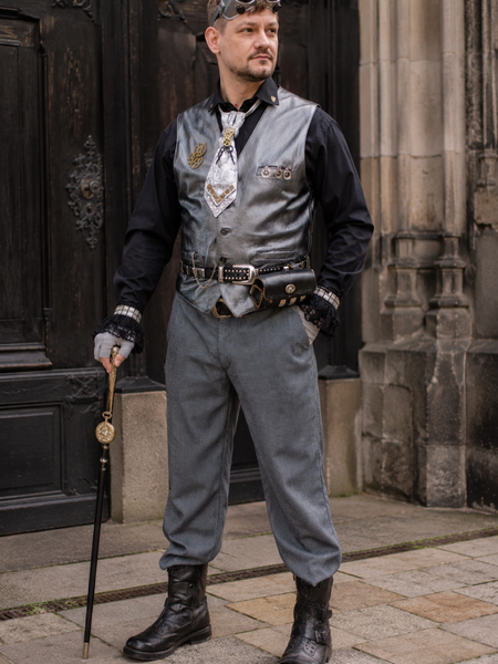 Steampunk Herren Outfit mit silberfarbener Lederweste, Goggles, Schurwollhose und Accessoires an echtem Modell vor historischem Gebäude.