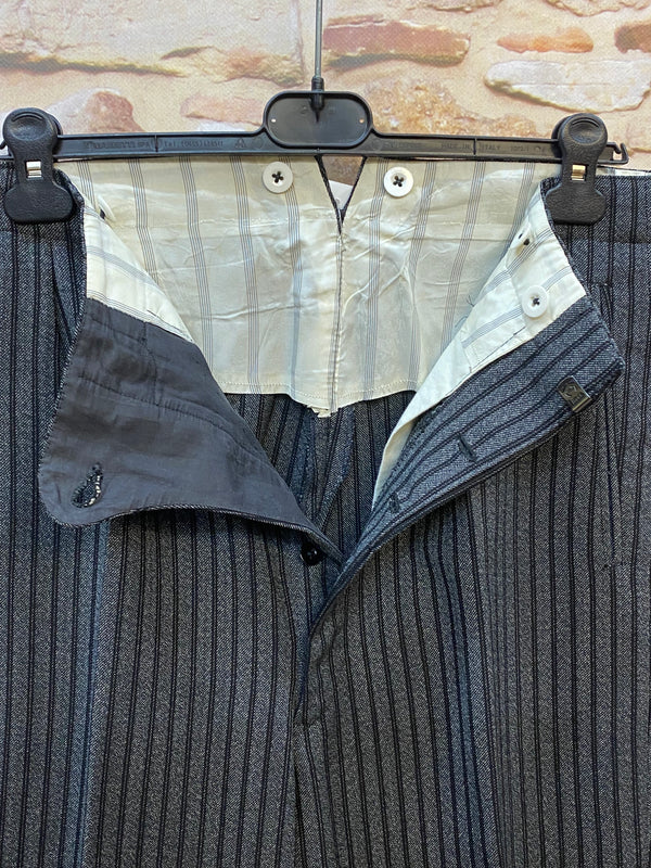 Antike gestreite Stresemann-Hose ein seltener Fund für Liebhaber klassischer Eleganz. In einem feinen grau-schwarzen Streifenmuster, handgefertigt aus reiner Schurwolle, ist sie ein Paradebeispiel für hochwertige Herrenmode. Die Hose ist mit Knöpfen ausgestattet, um Hosenträger anzubringen, Unikat