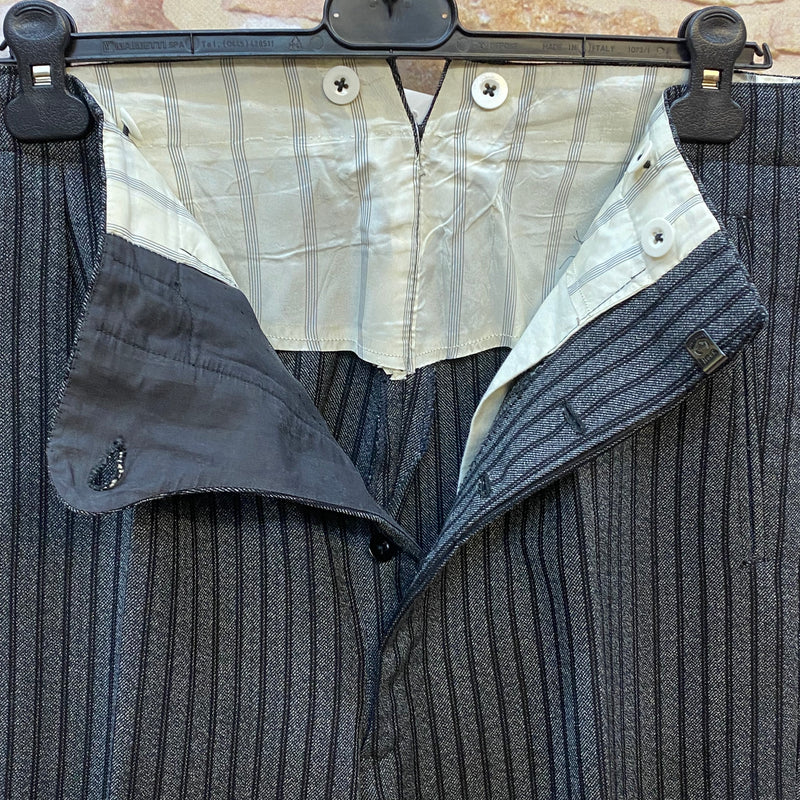 Antike gestreite Stresemann-Hose ein seltener Fund für Liebhaber klassischer Eleganz. In einem feinen grau-schwarzen Streifenmuster, handgefertigt aus reiner Schurwolle, ist sie ein Paradebeispiel für hochwertige Herrenmode. Die Hose ist mit Knöpfen ausgestattet, um Hosenträger anzubringen, Unikat