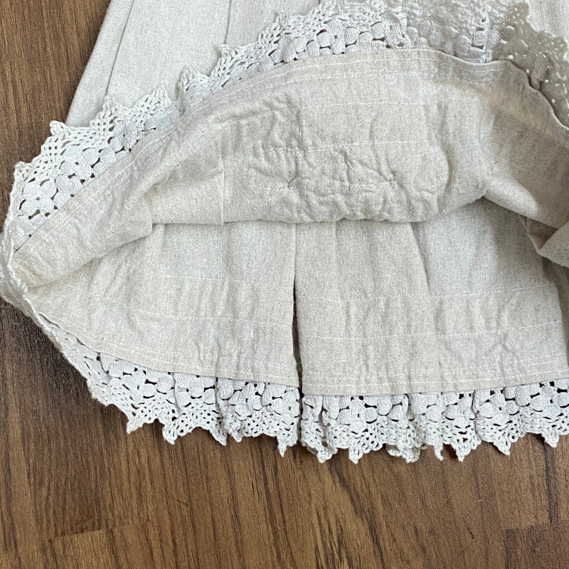 „Detailaufnahme der Klöppelspitze und Trachtenknöpfe am Rocksaum“