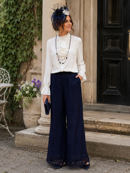 „Tragebeispiel 20er Jahre Damen Outfit mit dunkelblauer Marlenehose, cremeweißer Rüschenbluse und seitlichem Fascinator“