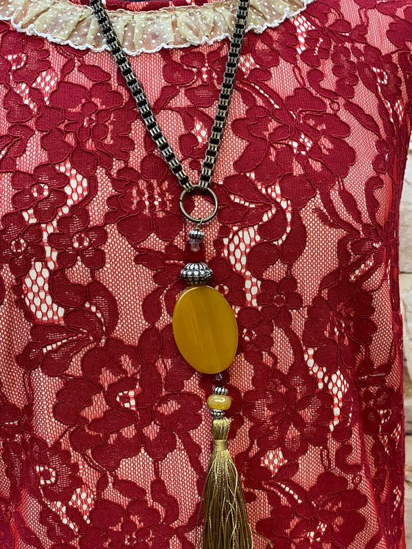 „Detailaufnahme rotes Spitzenkleid mit heller Rüschenbordüre, Stoffblüte und Vintage Kette mit Quaste“