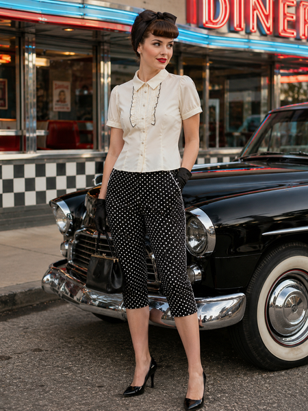 „Tragebeispiel 50er Jahre Damen Outfit mit gepunkteter Caprihose, cremeweißer Bluse, Haarband und Oldtimer“