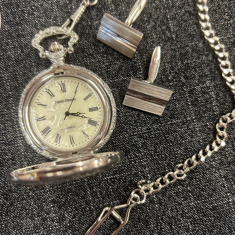 Silberne Taschenuhr und Manschettenknöpfe im Detail auf dunklem Hintergrund