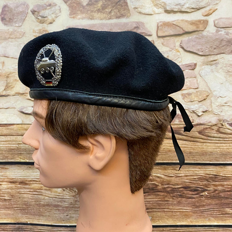 „Seitliche Ansicht von schwarzem Vintage Uniform-Barett mit Abzeichen, schwarzem Rand und Zugband“