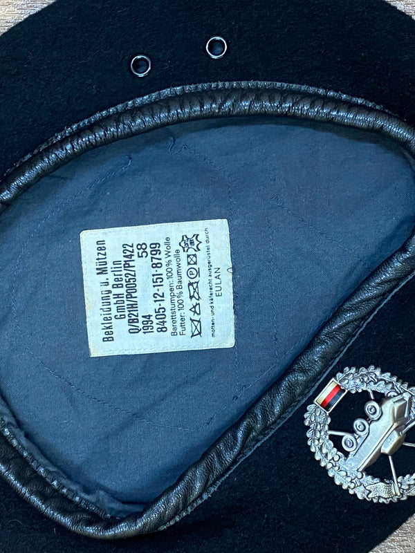 „Innenansicht eines schwarzen Vintage Uniform-Baretts Größe 58 mit dunklem Futter, Etikett und Metallabzeichen“