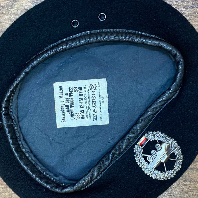 „Innenansicht eines schwarzen Vintage Uniform-Baretts Größe 58 mit dunklem Futter, Etikett und Metallabzeichen“