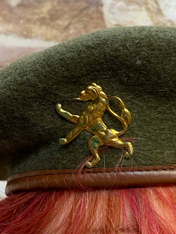 „Detailaufnahme vom goldfarbenen Löwen-Abzeichen auf grünem Vintage Barett“
